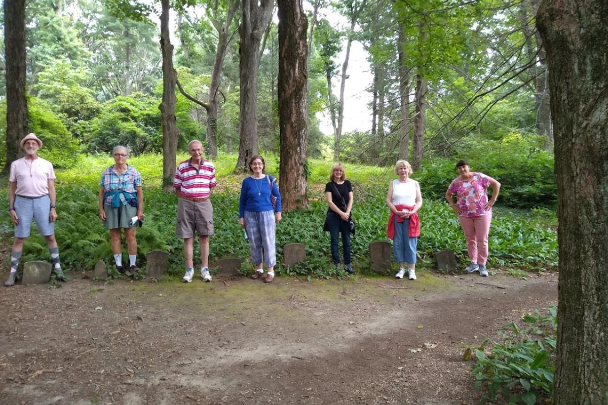 Five Visitors Stand Next to Graves during Hike in Maudslay State Park