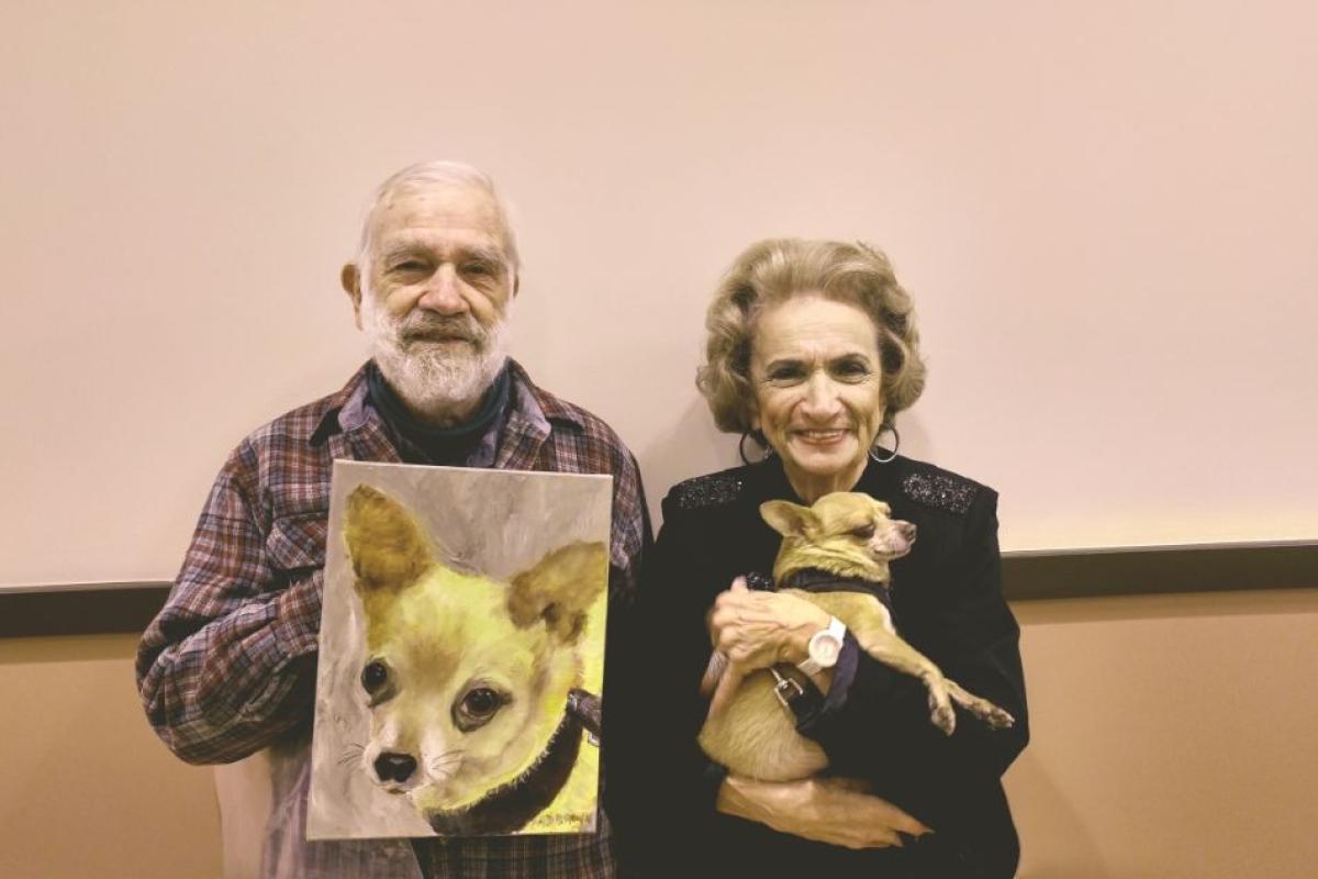 A Man is Holding a Painting of His Dog Next to the Female Artist Who Painted It