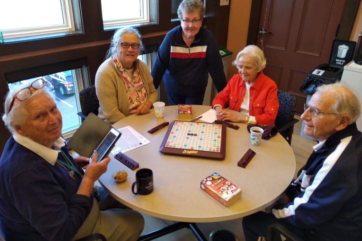 Five People Surround a Scrabble Board