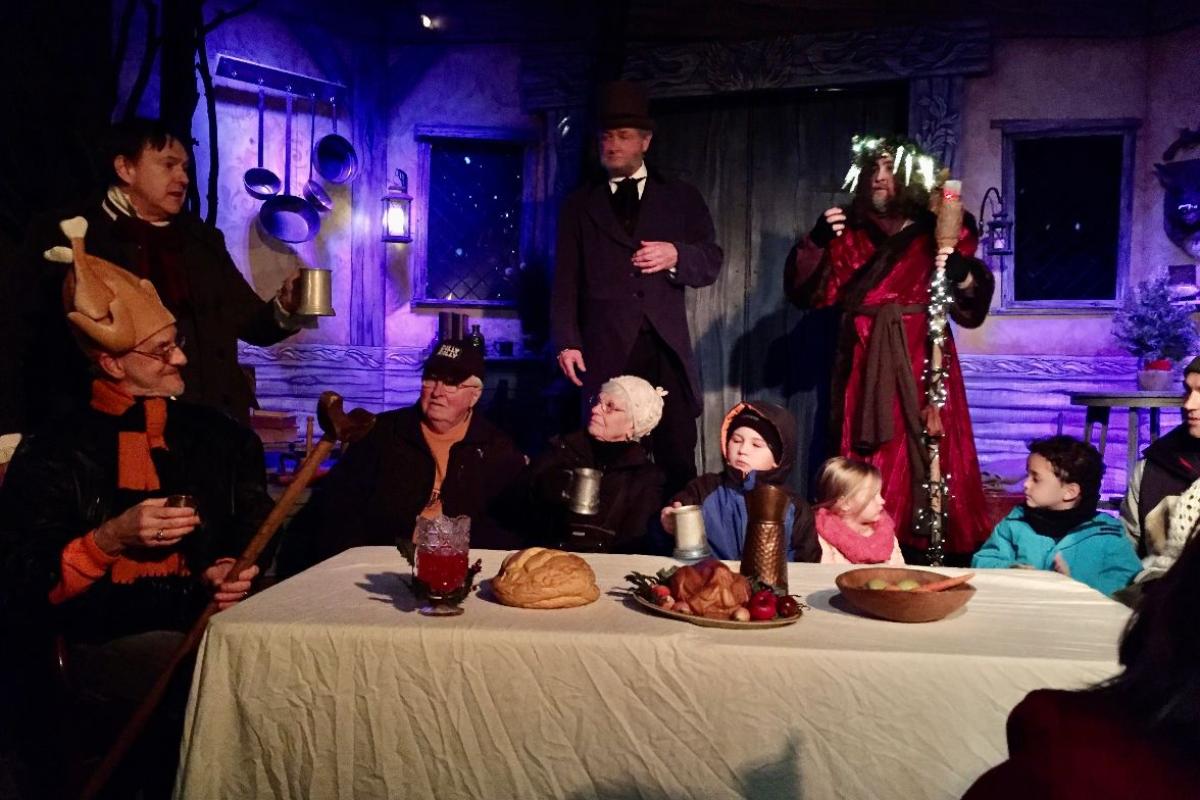 People Depicting the Kratchit Family Sit around the Christmas Dinner Table during a Stage Production